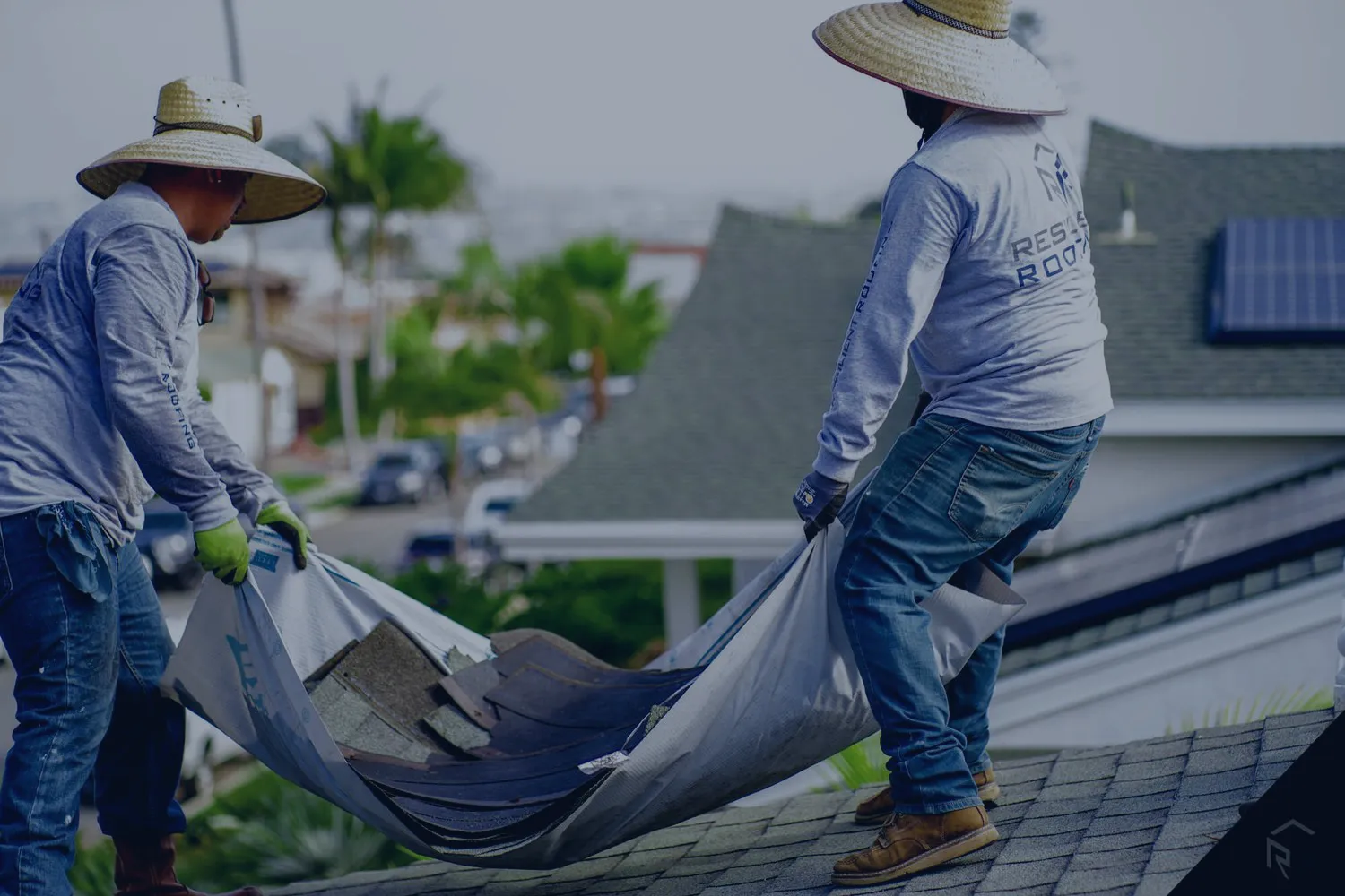 Two roofers carrying a tarp of torn-off shingle debris during a full roof tear-off.