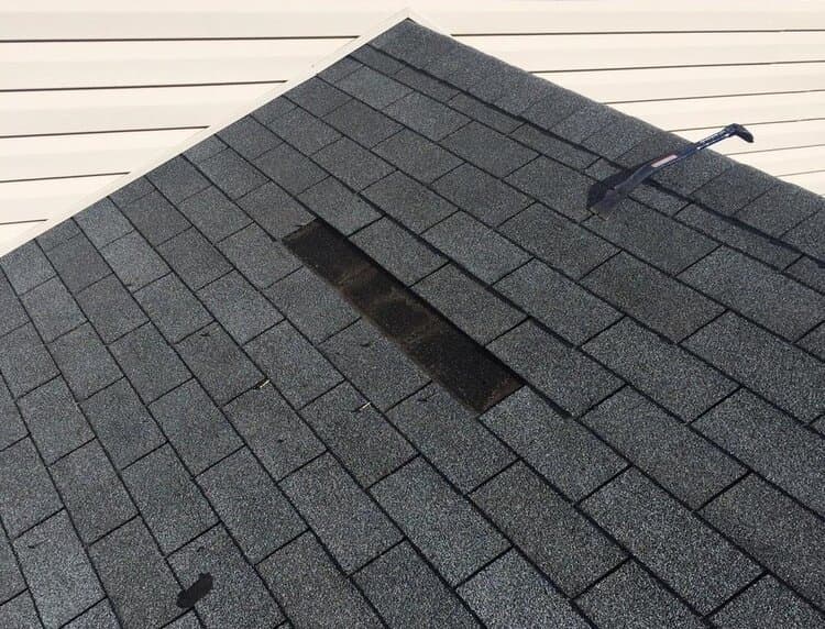A shingle roof with a section of shingles missing, exposing the underlayment after damage.
