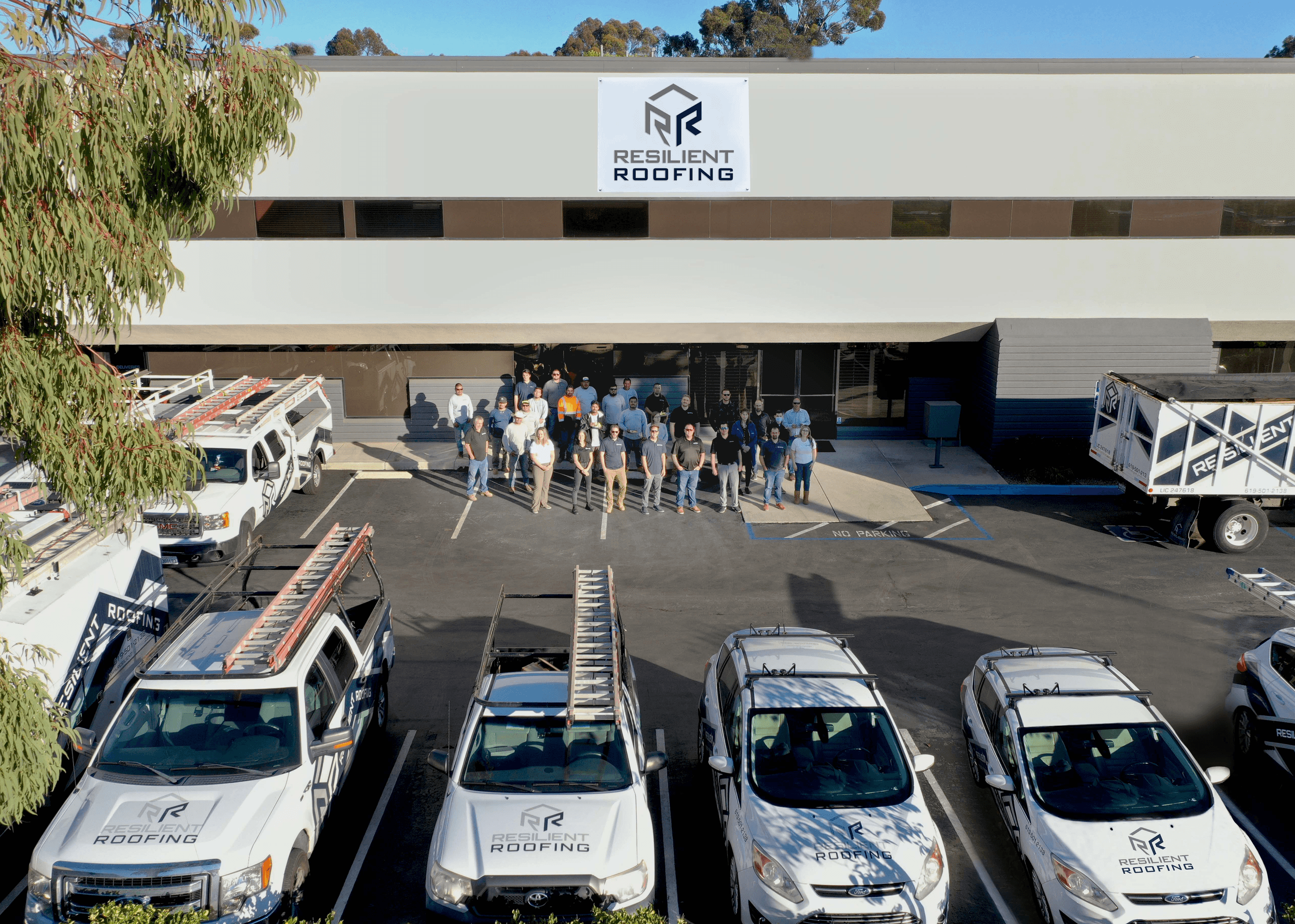 The Resilient Roofing team gathered with their branded trucks in front of the company building.